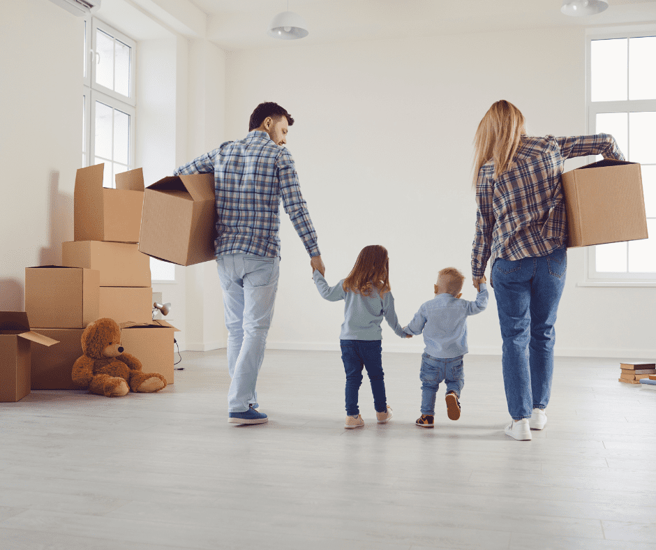 Back shot of a family. Parents carrying boxes and holding their children